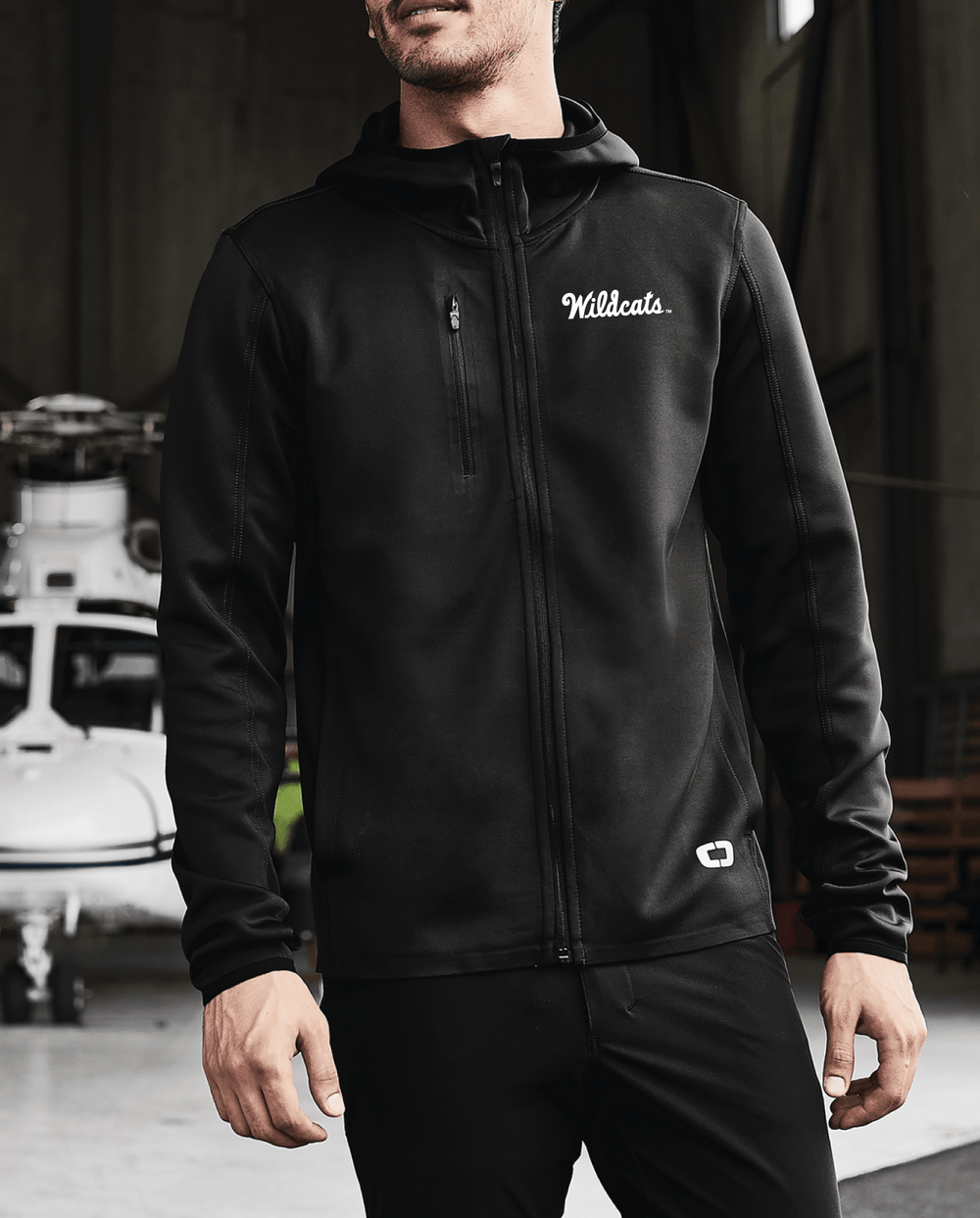 Lifestyle photo of a man wearing a black Kansas State performance OGIO jacket with the "Wildcats" logo embroidered in white thread on the left chest