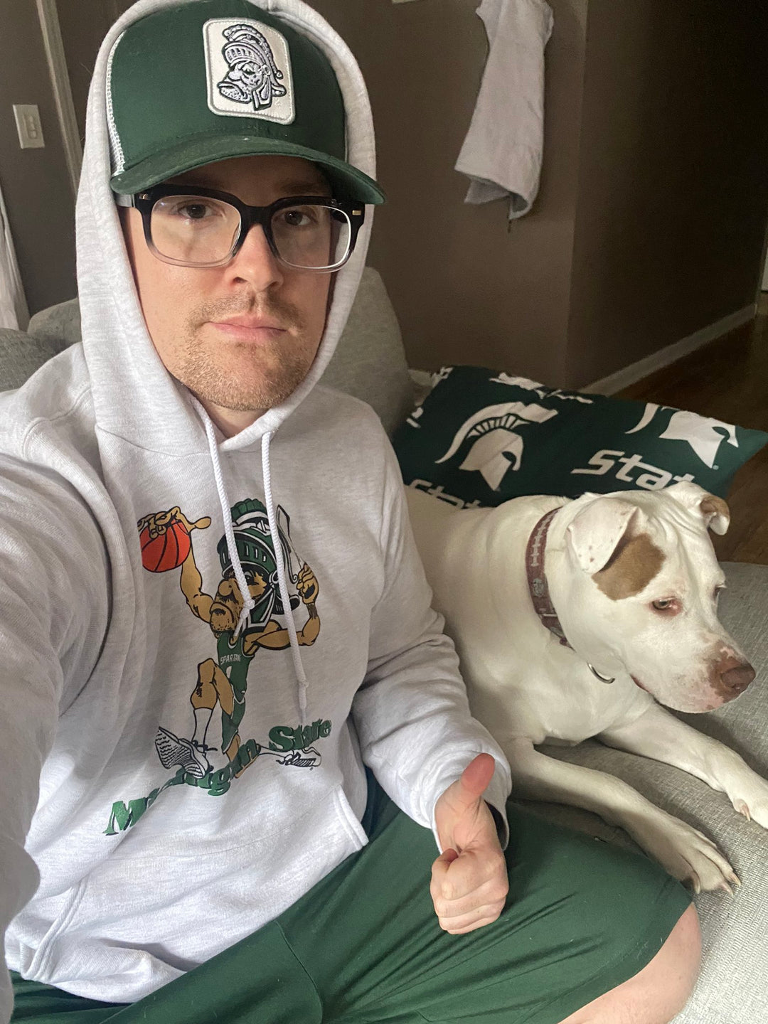 Michigan State Fan wearing MSU Spartans Dunking Gruff Sparty White hooded Sweatshirt with white dog next to him