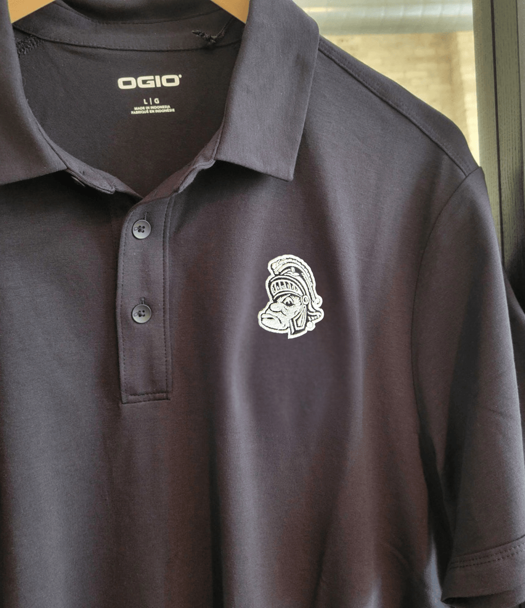 Black Michigan State Short Sleeve Polo with white Gruff Sparty logo on the left chest on male model on Hanger