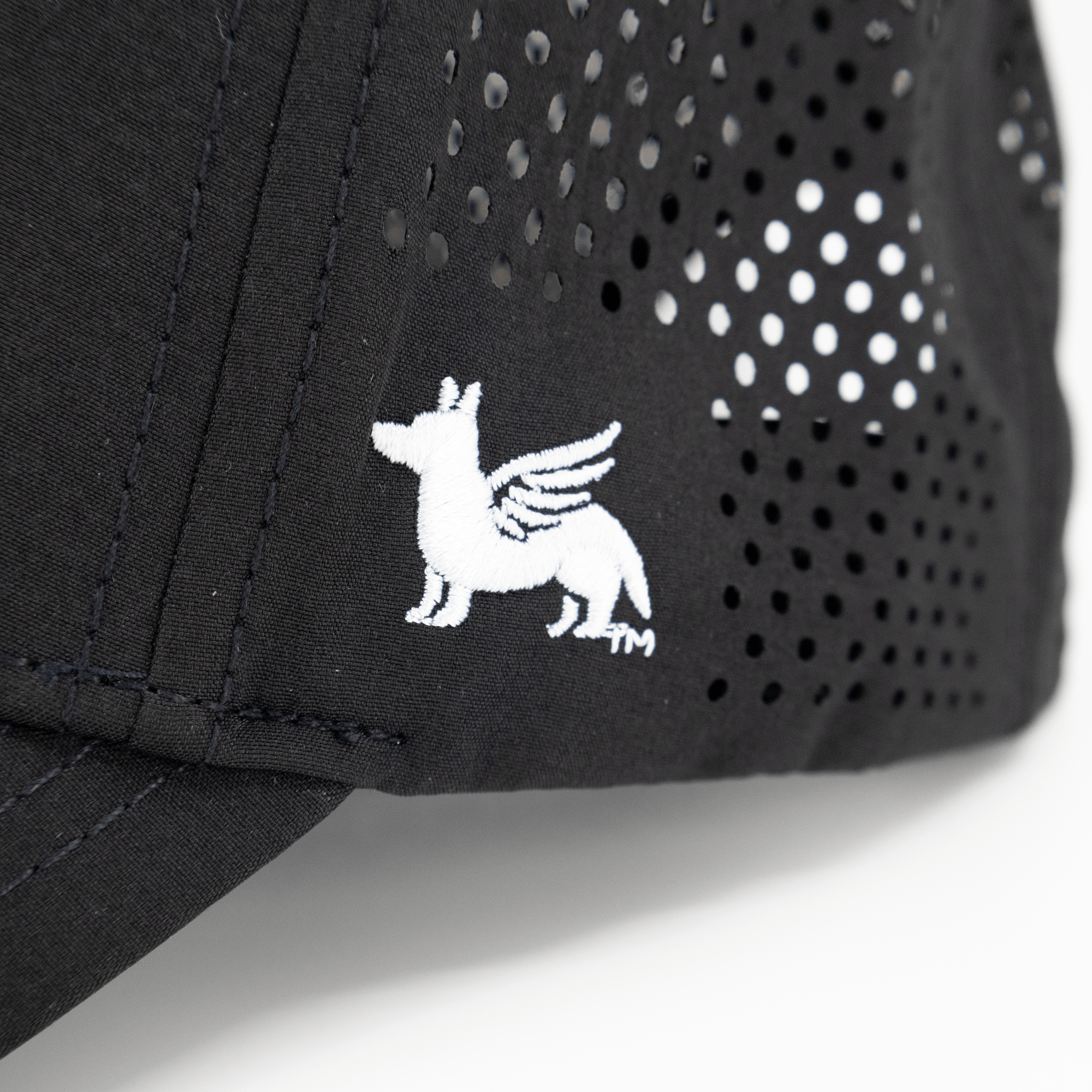 Close up view of a Nudge Printing black hat showing the logo in white thread.