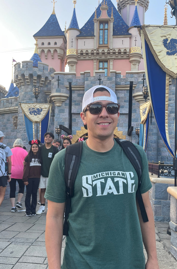Michigan State Green 2000 Champs Basketball Logo shirt on male model standing in front of the Castle at Disneyland