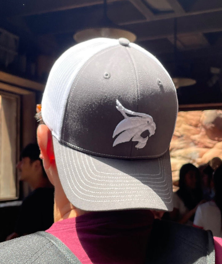 Model wearing backwards Texas State Bobcats Trucker hat that is grey in front and white mesh in back standing in line at Disneyland Up close