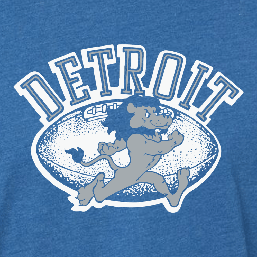 Close-up of vintage Detroit football t-shirt graphic featuring bold white 'Detroit' text, distressed football illustration, and cartoon running lion on heather blue fabric
