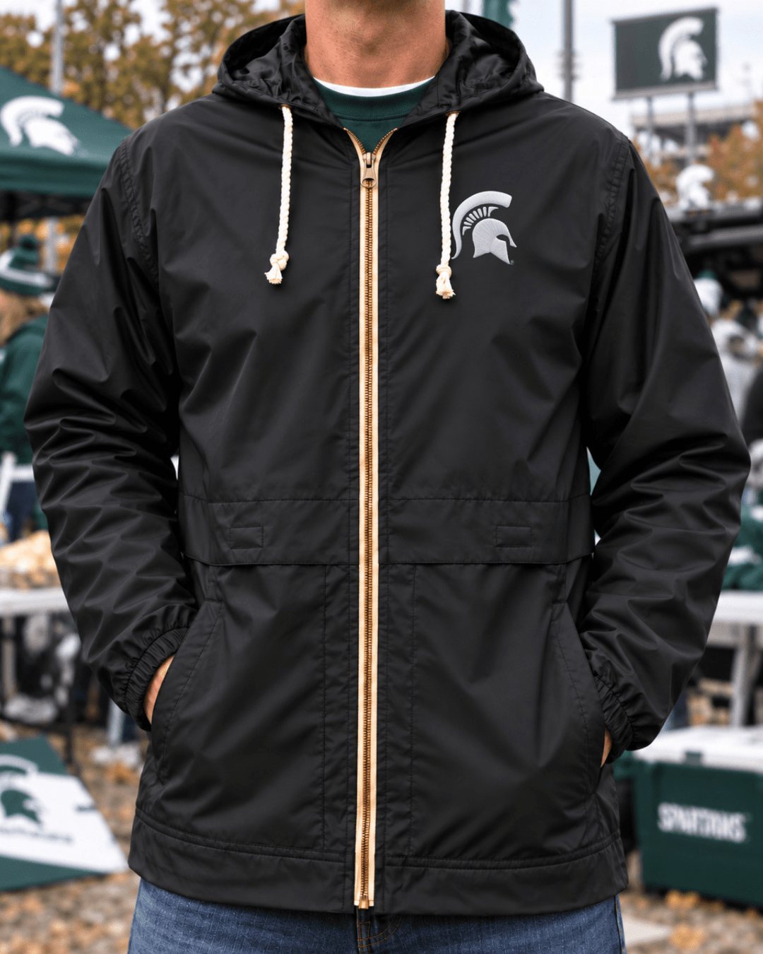 Image of male model wearing black Michigan State raincoat with hood outside Spartan Stadium.
