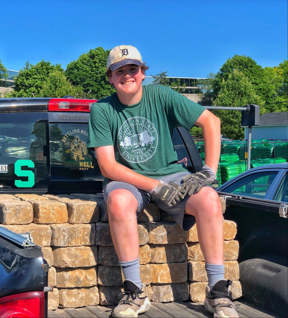 Michigan State Student wearing Official Seal Green MSU Shirt sitting on bricks in the back of a back truck