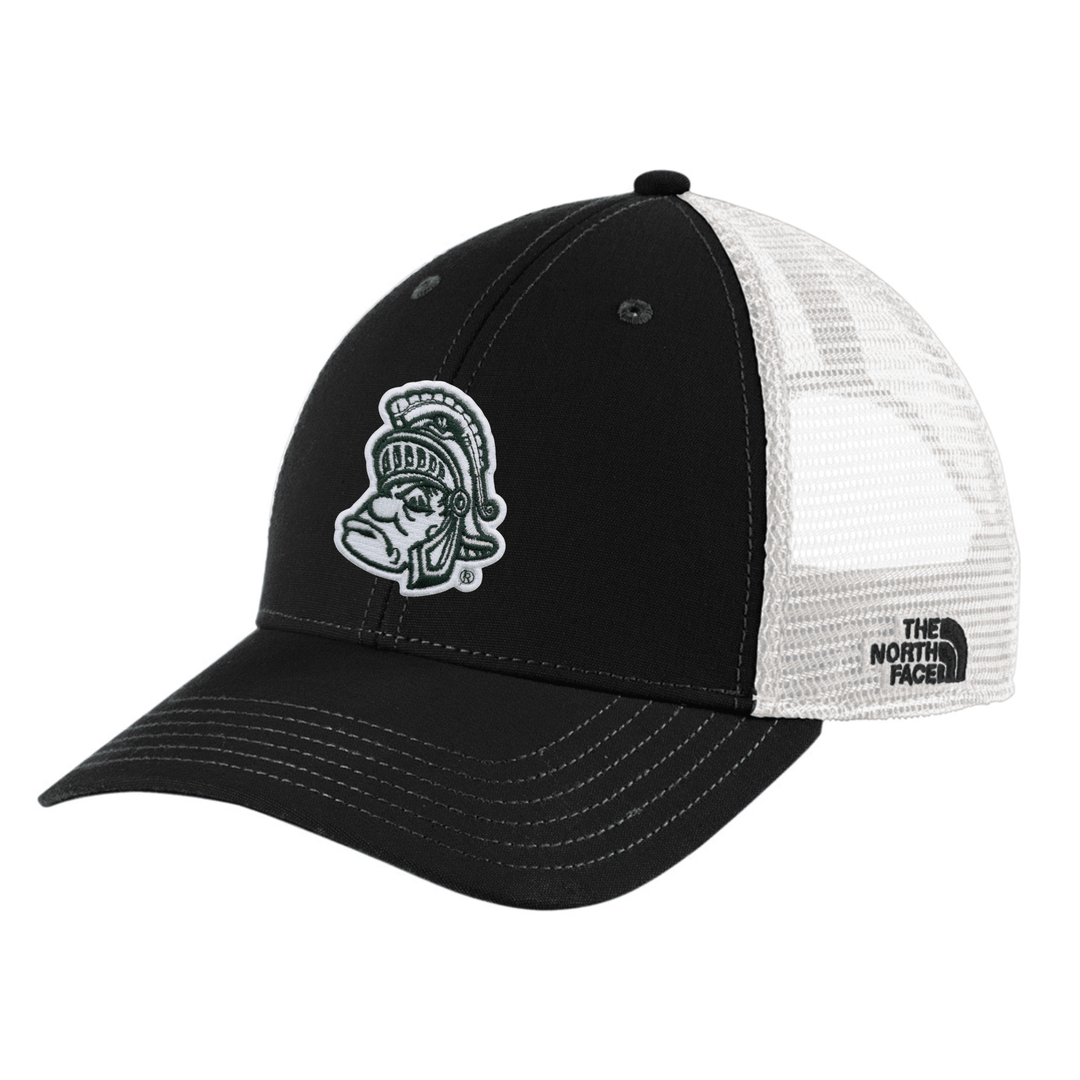 Angled view of black The North Face Michigan State trucker hat with embroidered Gruff Sparty patch on the front and white mesh back panels with The North Face brand label.