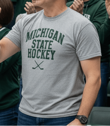 Man wearing a Michigan State Hockey grey shirt while watching the MSU Spartans play hockey at Munn Ice Arena