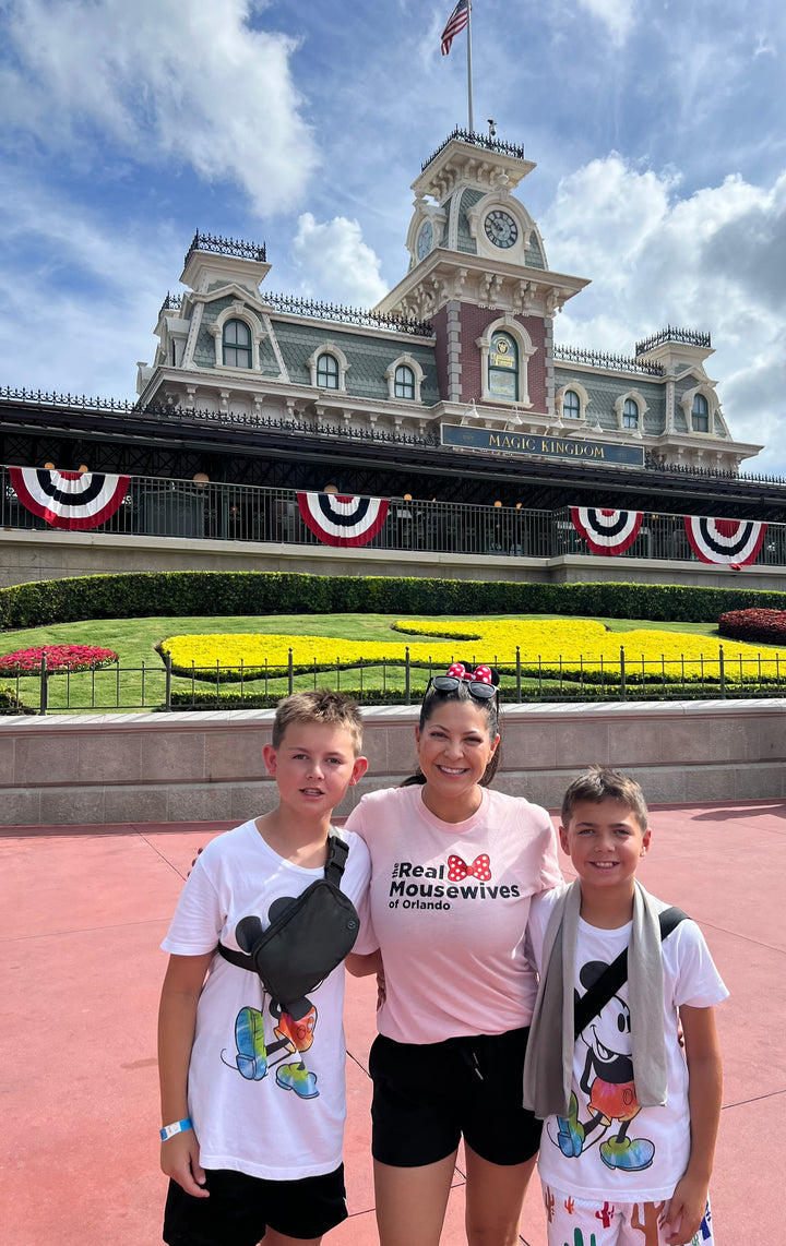 Female model wearing theme park t-shirt with the real mousewives of orlando pink shirt in front of Magic Kingdom
