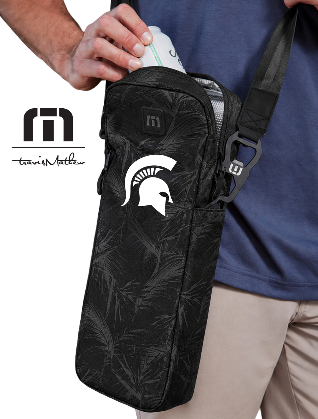 Man holding a black crossbody can cooler with a Michigan State University logo, wearing a blue shirt and beige shorts.