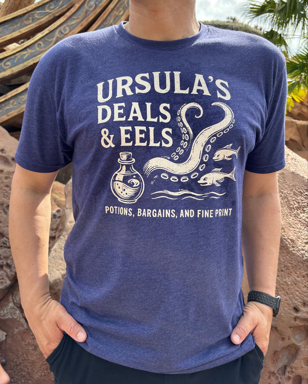 Ursula's Deals and Eels Purple Shirt on Male Model at Disney World at the Little Mermaid ride entrance with potion bottle and tentacles and eels 