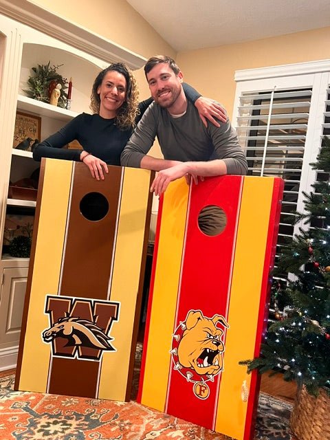 Picture of man and woman posing with 2 corn hole boards with Western Michigan and Ferris State University decals.